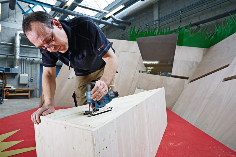 Eine Person verwendet eine Akku-Stichsäge, um in einer Werkstatt Holz zu schneiden. Anwendungsbild