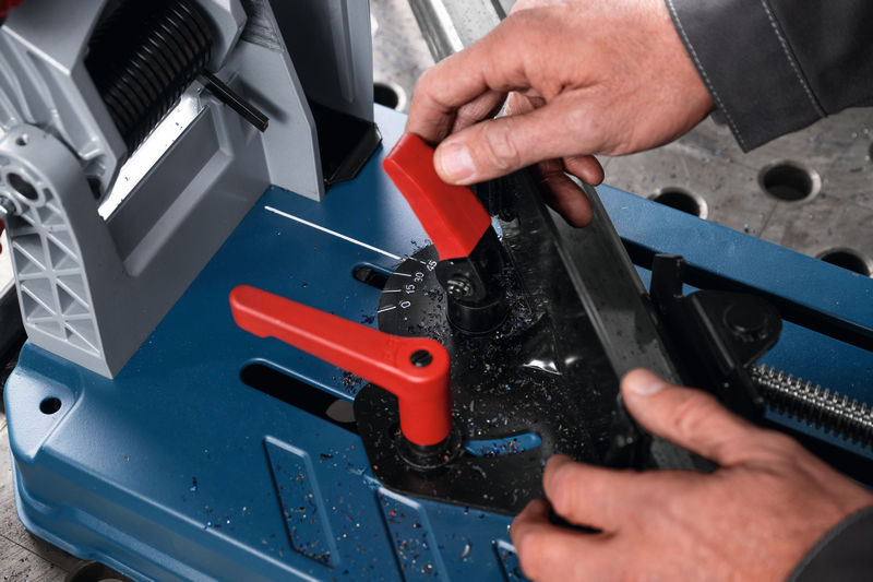 Eine Person stellt den Winkel einer Metalltrennsäge ein, Späne bedecken die blaue Basis. Anwendungsbild