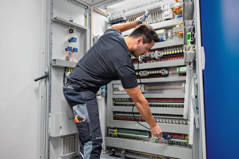Eine Person mit Sicherheitsausrüstung testet ein elektrisches Bedienfeld mit einem Spannungsprüfer. Anwendungsbild