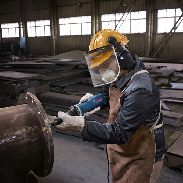 Eine Person mit Schutzausrüstung verwendet einen Geradschleifer an einem großen Metallrohr. Anwendungsbild