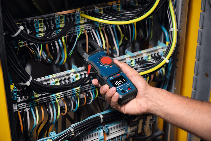 Eine Person verwendet ein Zangenmessgerät, um den Strom in einem elektrischen Bedienfeld zu messen. Anwendungsbild