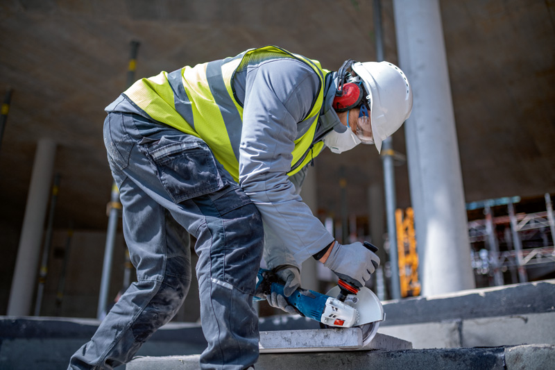 Eine Person mit Schutzausrüstung schleift Beton mit einem Akku-Winkelschleifer. Anwendungsbild