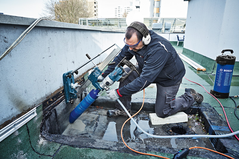 Eine Person mit Sicherheitsausrüstung bohrt mit einem montierten Diamantbohrer in Beton. Anwendungsbild