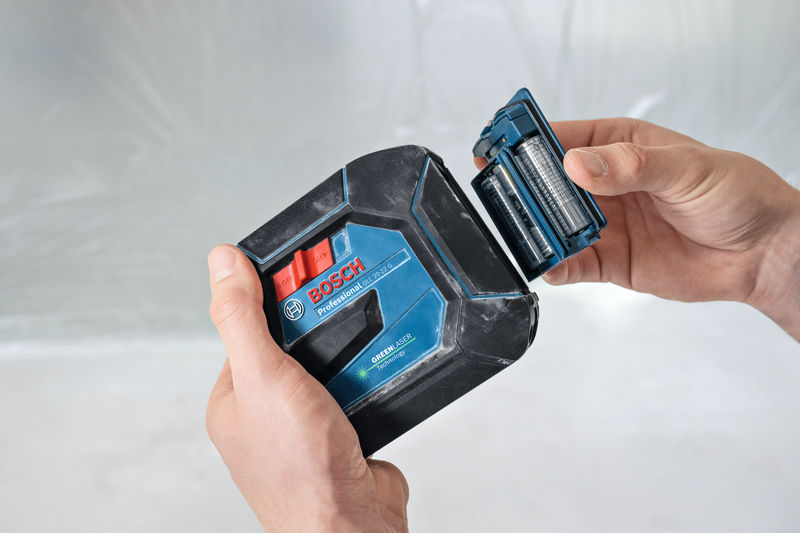 Eine Person tauscht die Batterien in einem grünen Lasernivelliergerät aus. Anwendungsbild