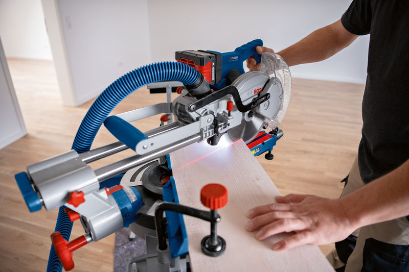 Eine Person verwendet eine kabellose Gehrungssäge zum Schneiden von Holz, geführt von einem Lasernivellierwerkzeug. Anwendungsbild