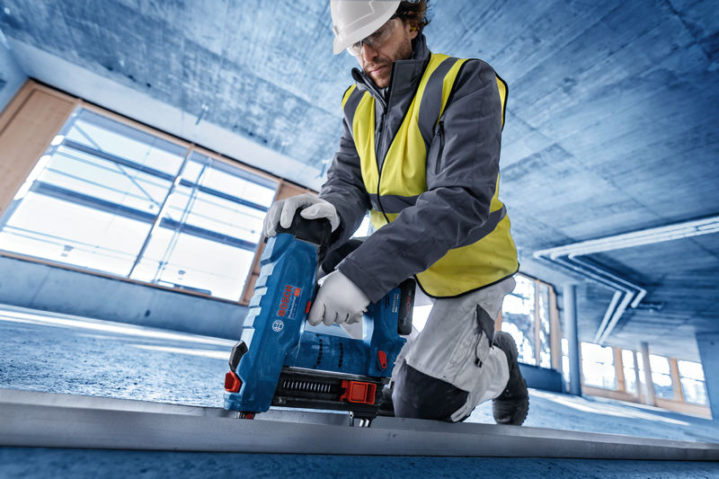 Eine Person mit Sicherheitsausrüstung bedient einen blauen Kernbohrer auf einem Betonboden. Anwendungsbild