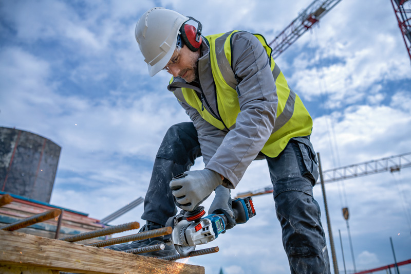 Eine Person mit Sicherheitsausrüstung schleift auf einer Baustelle Bewehrungsstahl mit einem Elektrowerkzeug. Anwendungsbild