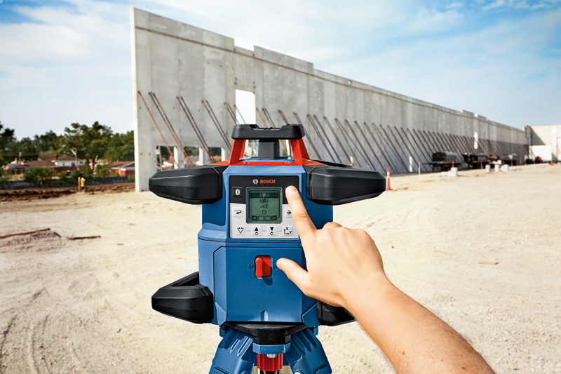 Person, die auf einer Baustelle mit großen Betonplatten ein Lasernivelliergerät bedient. Anwendungsbild