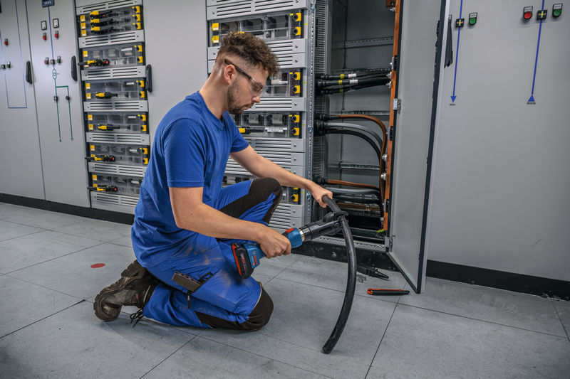 Eine Person mit Sicherheitsausrüstung verwendet ein kabelloses hydraulisches Schneidwerkzeug an einem dicken Kabel. Anwendungsbild