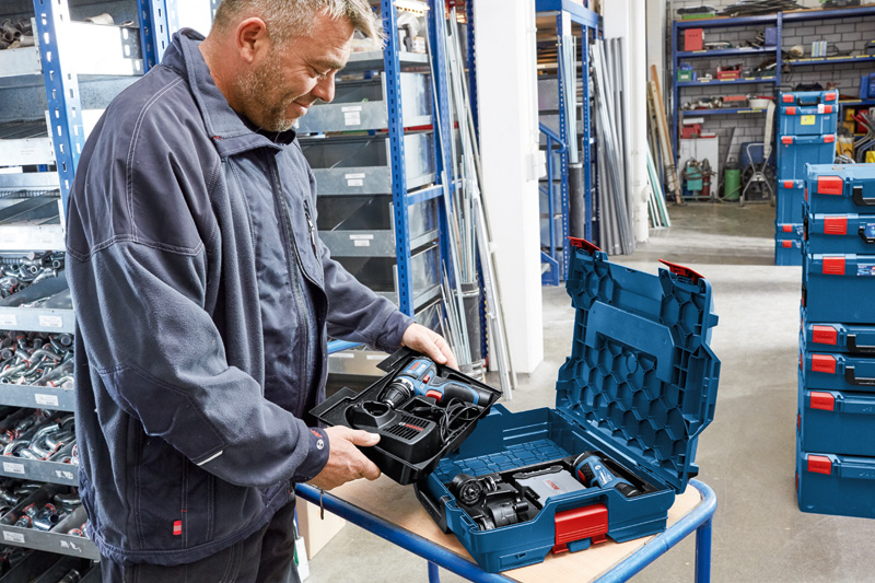 Eine Person in einer Werkstatt packt ein Akku-Werkzeugset aus einem Hartplastikkoffer aus. Anwendungsbild