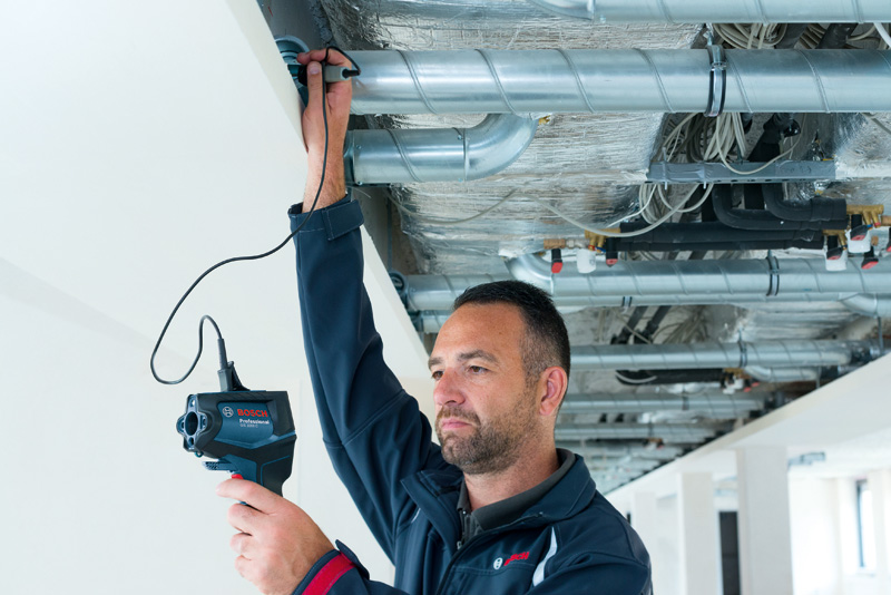 Eine Person verwendet einen Thermodetektor, um HVAC-Rohre an einer Decke zu überprüfen. Anwendungsbild
