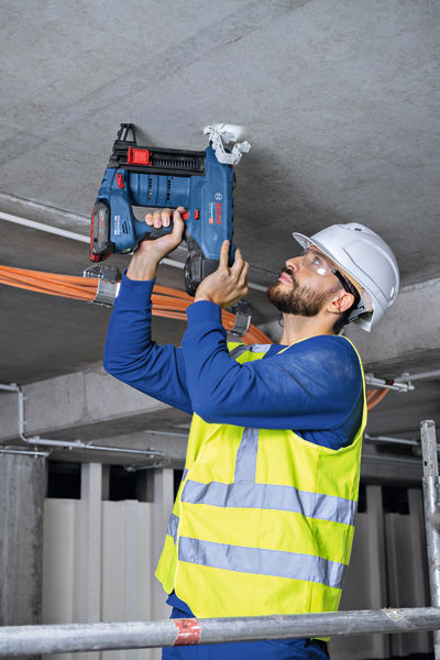 Eine Person mit Sicherheitsausrüstung befestigt mit einem Akkunagler Kabelhalterungen über Kopf. Anwendungsbild