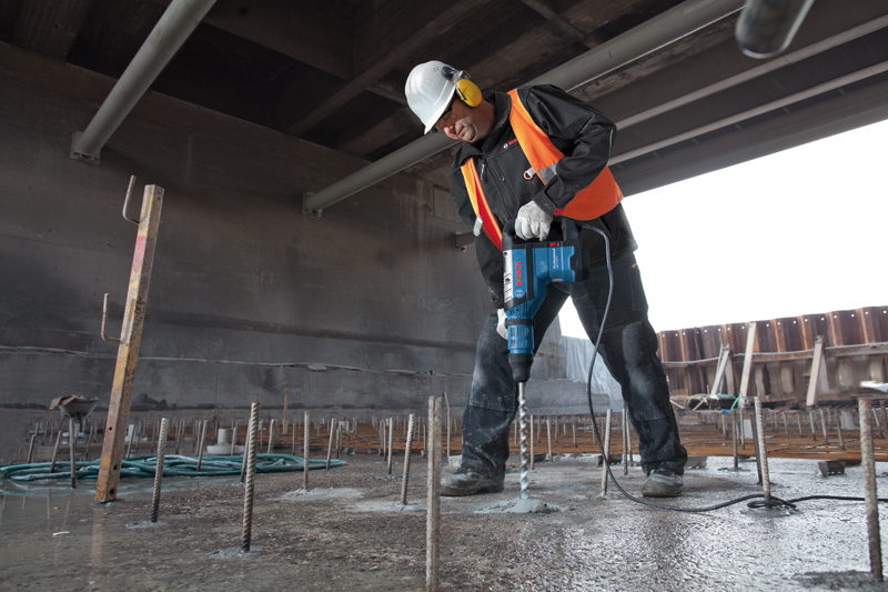 Eine Person mit Sicherheitsausrüstung bohrt auf einer Baustelle mit einem Bohrhammer in Beton. Anwendungsbild