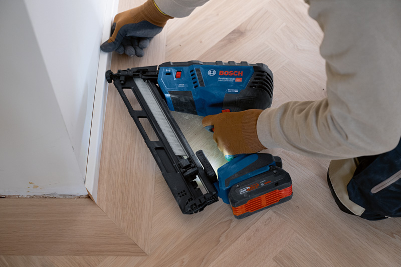Eine Person mit Sicherheitsausrüstung befestigt mit einem Akku-Holznagler Zierleisten auf einem Holzboden. Anwendungsbild