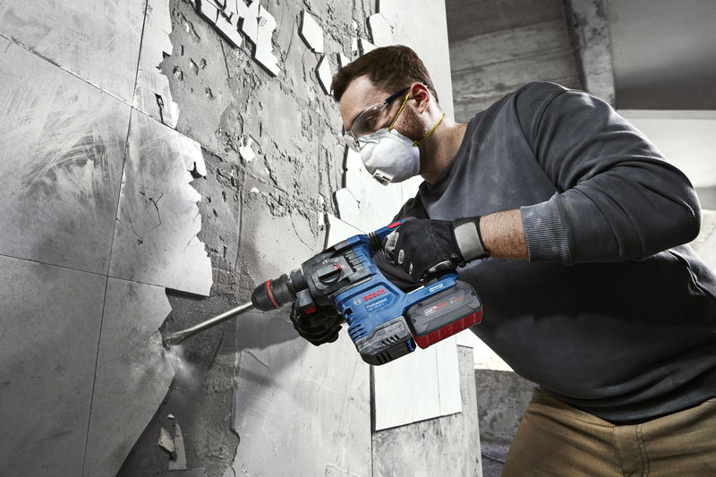 Eine Person mit Schutzausrüstung entfernt mit einem Bohrhammer Fliesen aus einer Wand. Anwendungsbild