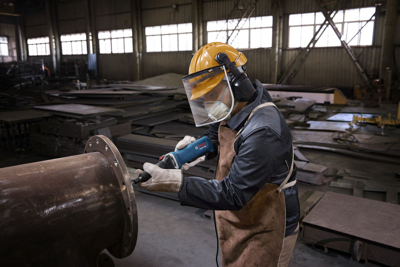 Eine Person mit Schutzausrüstung bearbeitet mit einem Geradschleifer ein großes Metallrohr. Anwendungsbild