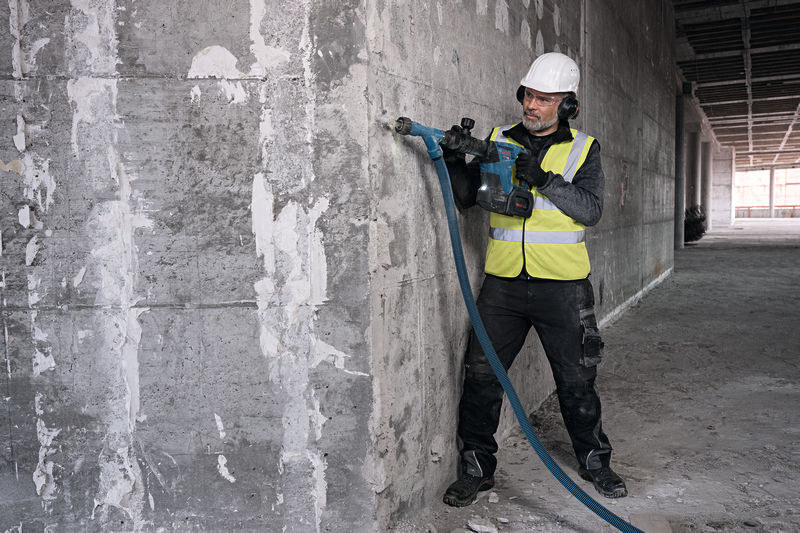 Eine Person mit Schutzausrüstung bearbeitet eine Betonwand mit einem Akku-Abbruchhammer. Anwendungsbild