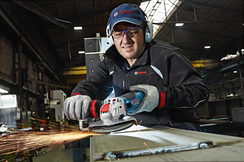 Eine Person mit Schutzausrüstung schleift Metall mit einem Winkelschleifer, Funken fliegen. Anwendungsbild