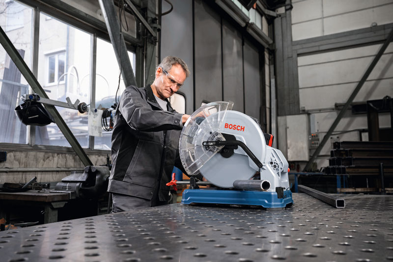 Eine Person mit Schutzausrüstung bedient in einer Werkstatt eine Metalltrennsäge. Anwendungsbild