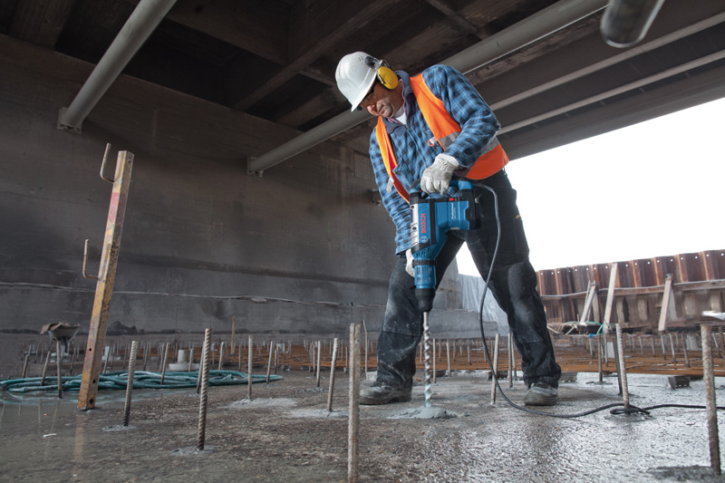Eine Person mit Schutzausrüstung bohrt mit einem Bohrhammer in Beton. Anwendungsbild
