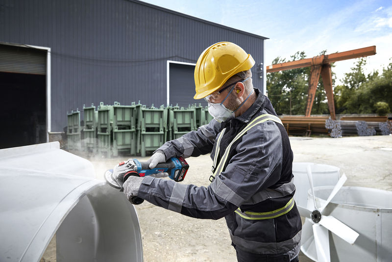 Eine Person mit Sicherheitsausrüstung schleift im Freien auf einem Industriegelände Metall. Anwendungsbild