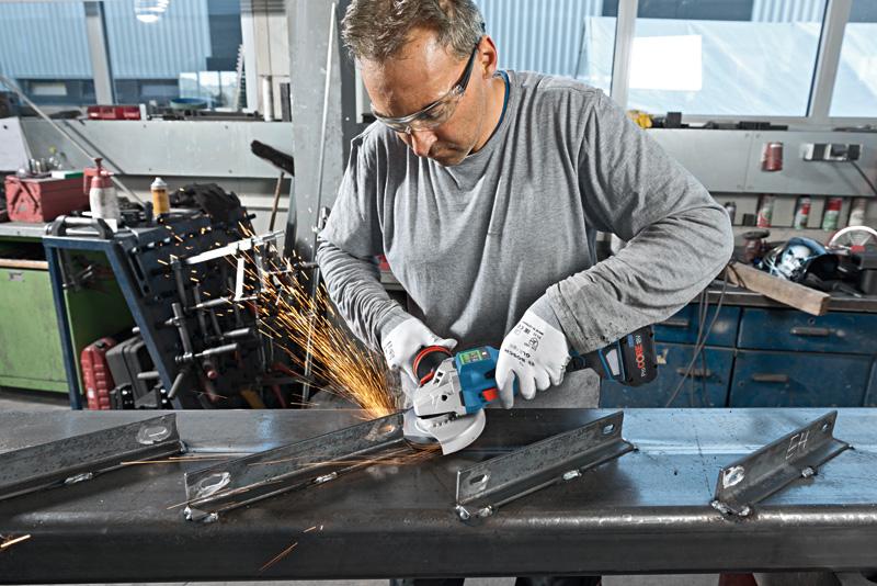 Eine Person mit Sicherheitsausrüstung schneidet mit einem Winkelschleifer einen Metallträger. Anwendungsbild