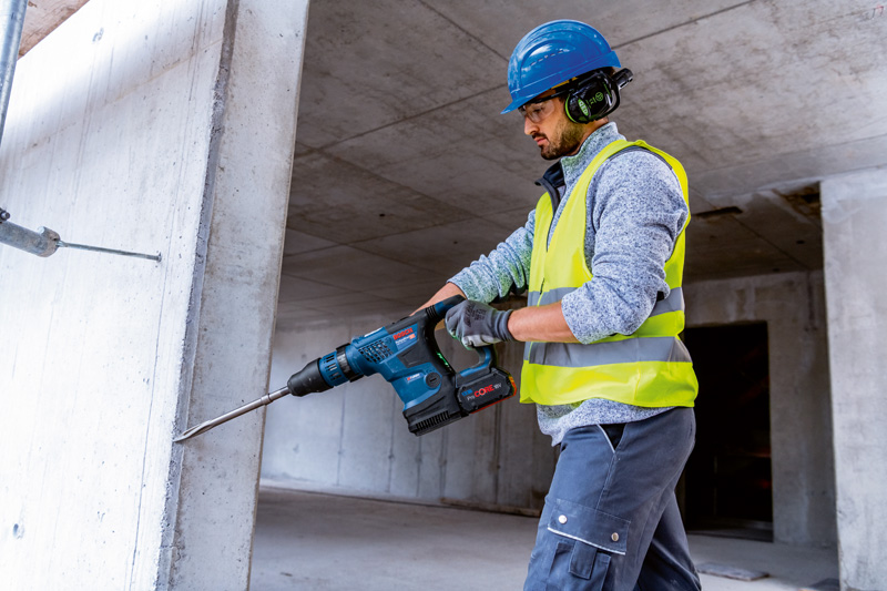 Eine Person mit Schutzausrüstung bohrt mit einem Akku-Bohrhammer in eine Betonwand. Anwendungsbild