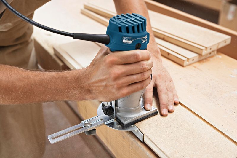 Eine Person verwendet eine Handfräse, um die Kante eines Holzbretts zu formen. Anwendungsbild