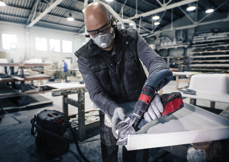 Ein Arbeiter mit Sicherheitsausrüstung schneidet in einer Werkstatt mit einem Elektrowerkzeug eine Arbeitsplatte. Anwendungsbild