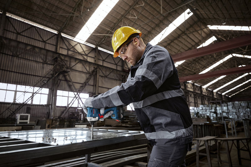 Eine Person mit Sicherheitsausrüstung befestigt mit einem Elektrowerkzeug Schrauben an einem Metallrahmen. Anwendungsbild