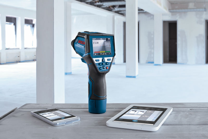 Thermodetektor mit digitaler Anzeige steht auf einem Tisch neben zwei Tablets in einem unfertigen Raum. Anwendungsbild