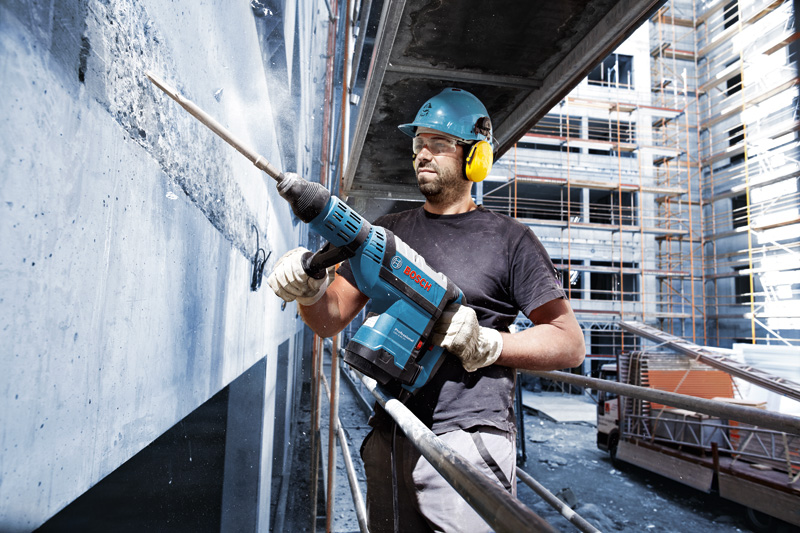 Eine Person mit Sicherheitsausrüstung verwendet einen Bohrhammer, um auf einer Baustelle Beton aufzubrechen. Anwendungsbild