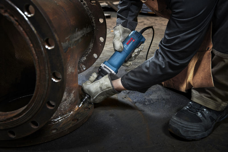 Eine Person mit Schutzausrüstung verwendet einen Geradschleifer an einem großen Metallflansch. Anwendungsbild