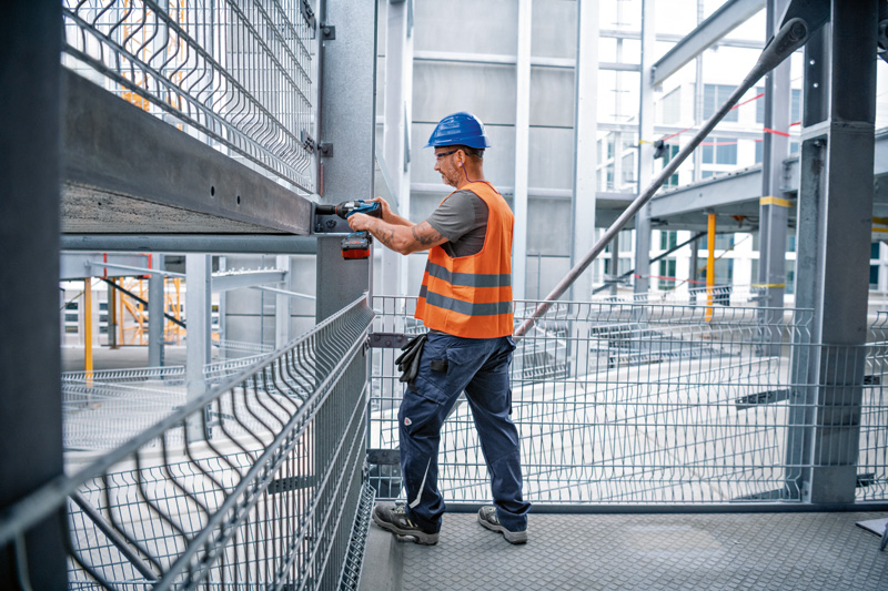 Eine Person mit Sicherheitsausrüstung verwendet auf einer Baustelle einen Schlagschrauber an einem Stahlträger. Anwendungsbild