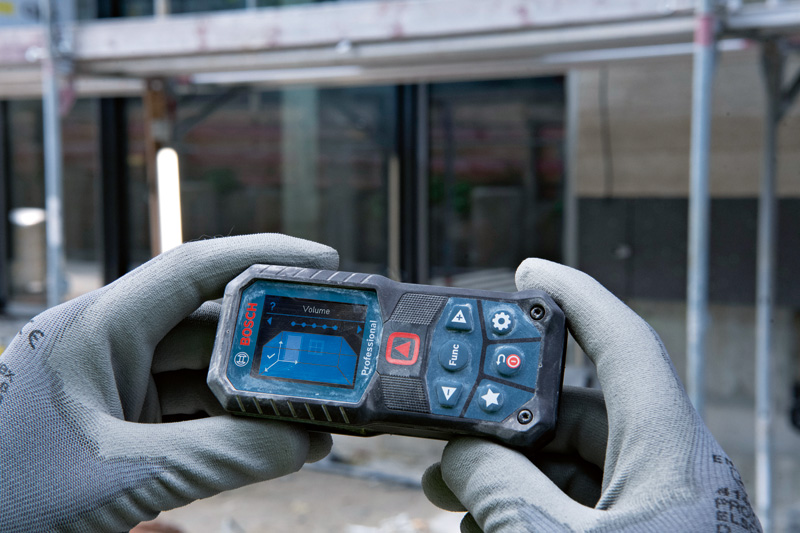 Eine Person mit Sicherheitsausrüstung bedient auf einer Baustelle ein Lasermessgerät. Anwendungsbild