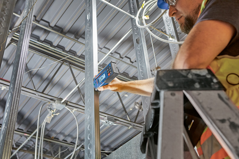 Eine Person mit Schutzausrüstung richtet mithilfe eines Laserempfängers einen Metallrahmen aus. Anwendungsbild