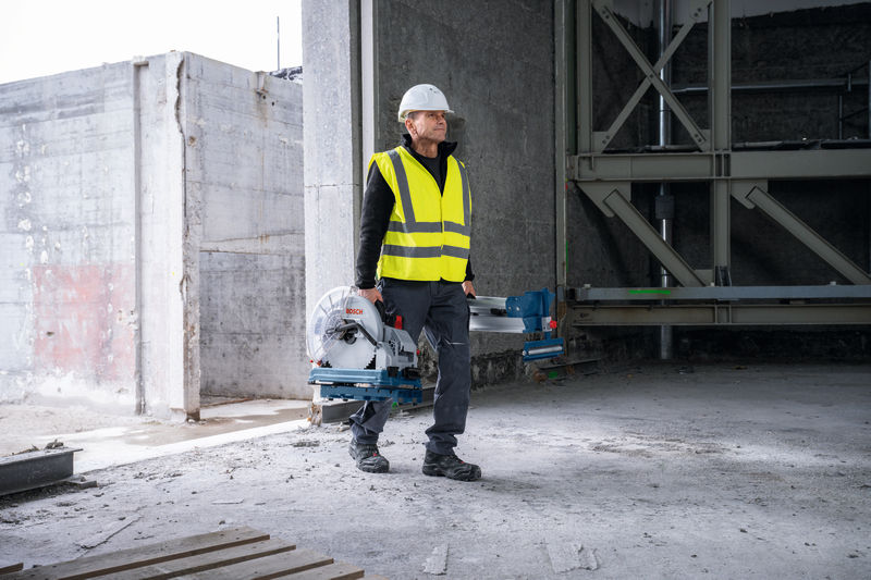 Eine Person mit Sicherheitsausrüstung trägt eine Metalltrennsäge in einem unfertigen Gebäude. Anwendungsbild