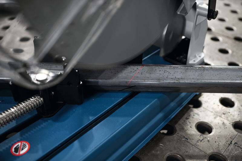 Metalltrennsäge mit roter Führungslinie schneidet eine Stahlstange auf einer perforierten Werkbank. Anwendungsbild