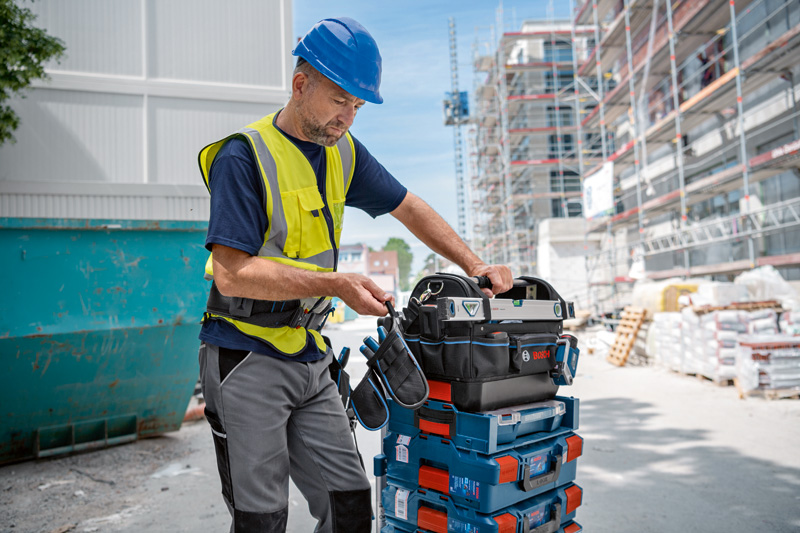 Eine Person mit Sicherheitsausrüstung ordnet Werkzeugkästen auf einer Baustelle. Anwendungsbild