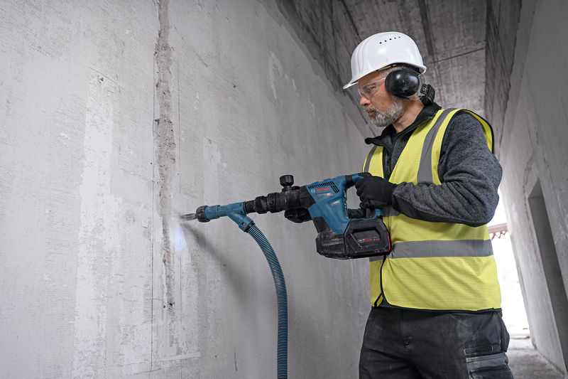Eine Person mit Schutzausrüstung bearbeitet eine Betonwand mit einem Akku-Abbruchhammer. Anwendungsbild