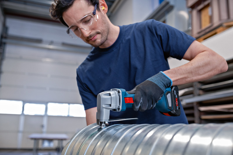 Eine Person mit Sicherheitsausrüstung schneidet mit einer kabellosen Metallschere einen Metallkanal durch. Anwendungsbild