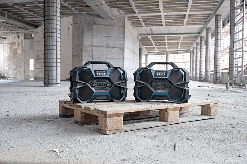 Zwei robuste Bauradios stehen auf einer Holzpalette auf einer Baustelle. Anwendungsbild