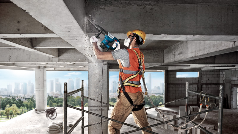 Eine Person mit Sicherheitsausrüstung zerstört mit einem Abbruchhammer eine Betonsäule. Anwendungsbild