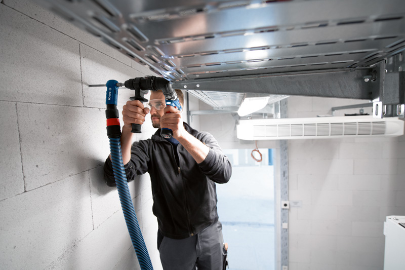 Eine Person mit Sicherheitsausrüstung bohrt mit einem FlexiClick-Adapter in eine Betonwand. Anwendungsbild