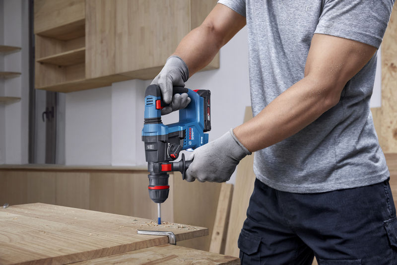 Eine Person mit Schutzausrüstung bohrt mit einem Akku-Bohrhammer in Holz. Anwendungsbild