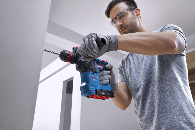 Eine Person mit Schutzausrüstung bohrt mit einem Akku-Bohrhammer in eine Betonwand. Anwendungsbild