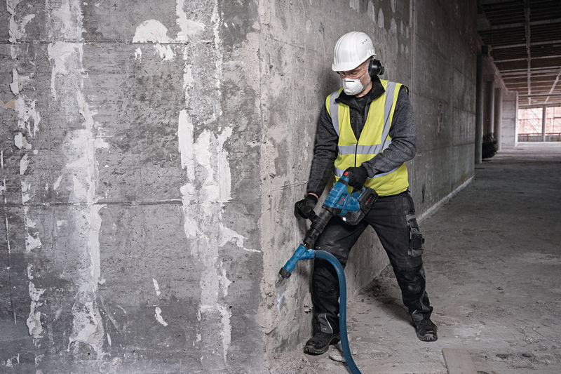 Eine Person mit Schutzausrüstung bearbeitet eine Betonwand mit einem Akku-Abbruchhammer. Anwendungsbild
