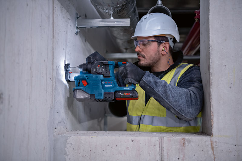 Eine Person mit Sicherheitsausrüstung bohrt mit einem Bohrhammer in Beton. Anwendungsbild