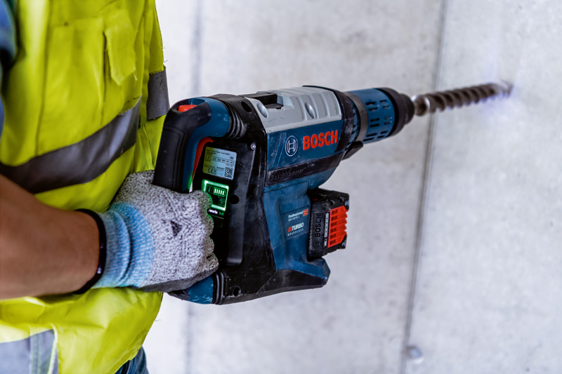 Eine Person mit Schutzausrüstung bohrt mit einem großen Bohrhammer in Beton. Anwendungsbild