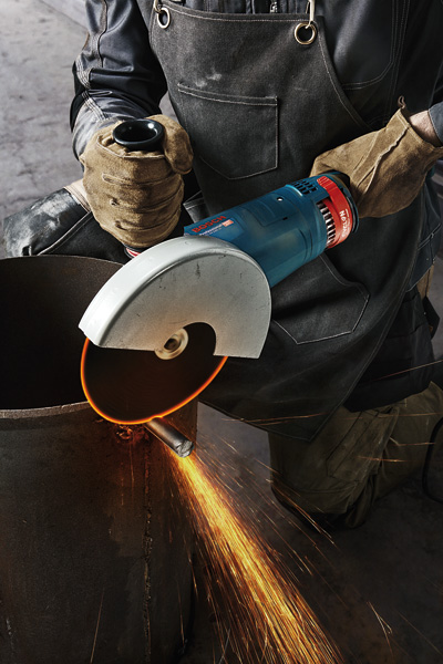 Eine Person mit Schutzausrüstung schneidet mit einem großen Winkelschleifer ein Metallrohr, Funken fliegen. Anwendungsbild Nahaufnahme